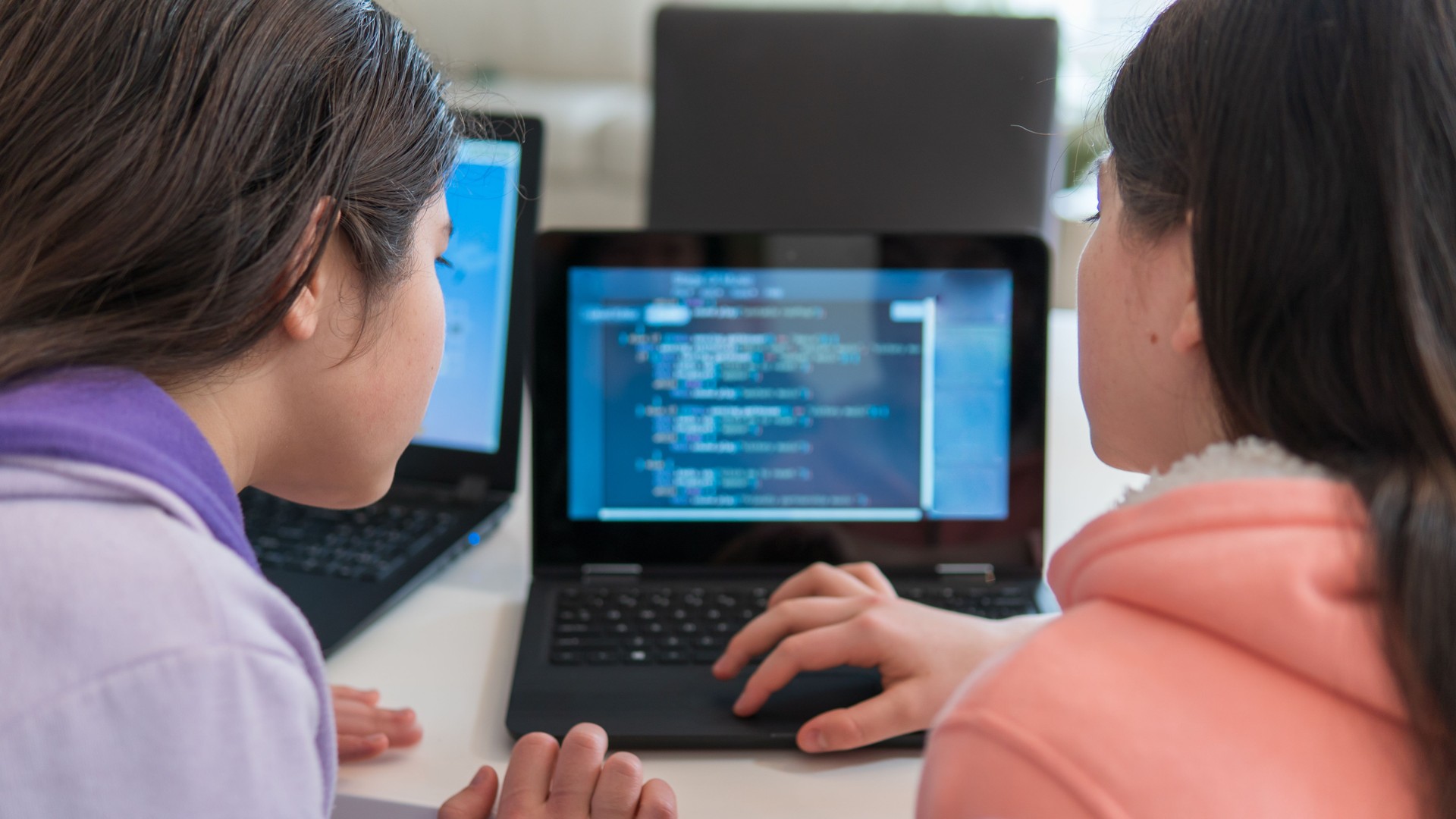 Girls learning to code on laptop computers at home